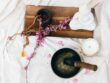 Flat lay of a meditation setup with a singing bowl, candle, beaded mala, and flower branch.
